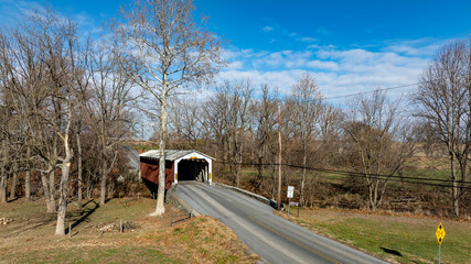 A charming covered bridge crosses a peaceful road surrounded by bare trees. The crisp morning air...