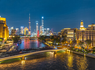 Panoramic view of the illuminated Shanghai city skyline with modern skyscrapers and historic buildings along the river at night in China.