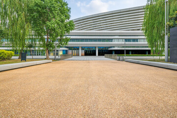 Empty textured pathway leading to the entrance of a modern building facade with green willow trees...