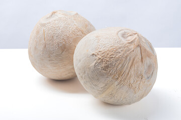 Two peeled young coconuts placed on a clean white surface with soft background, showing rough...