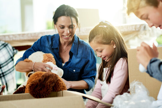 Moving, boxes and mother with children for packing in new home with sorting toys for donation or charity. Cardboard, fun and mom helping kids with teddy bear or trinkets for relocation in house.