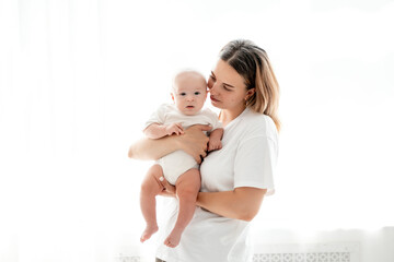 happy mom with a newborn baby on a white isolated background, space for text, mom hugs and kisses her baby while holding him in her arms, happy motherhood