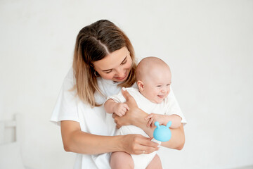 mom and baby, mother hold a newborn baby in her arms at home in the bedroom, hugging him, playing with him with a rattle, maternal care and love, portrait of a happy mother with a child.