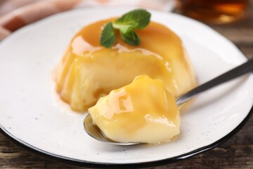 Delicious pudding with caramel sauce and mint served on wooden table, closeup