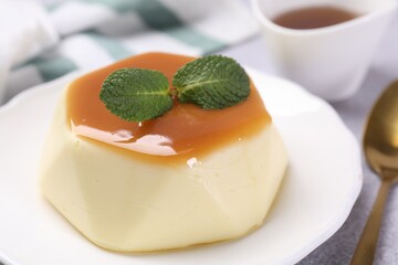 Delicious pudding with caramel sauce and mint served on light table, closeup