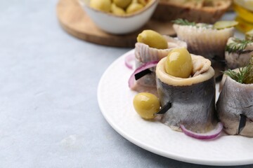 Delicious herring rolls with olives, pickles, dill and onion on gray table, closeup. Space for text