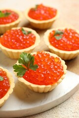 Tartlets with red caviar and parsley on beige table, closeup