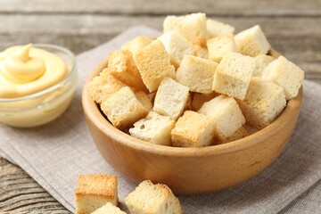 Tasty crispy croutons in bowl and sauce on wooden table, closeup