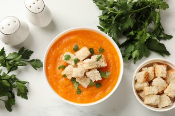 Delicious pumpkin cream soup with croutons, parsley and ingredients on white table, flat lay
