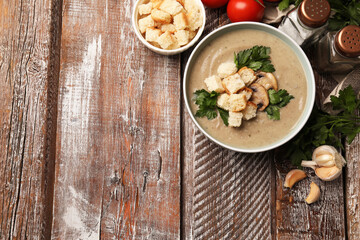 Delicious mushroom cream soup with croutons and ingredients on wooden table, flat lay. Space for text