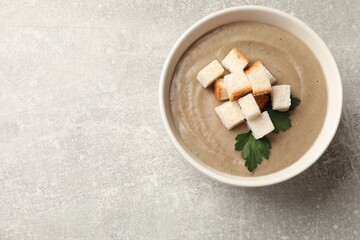 Delicious mushroom cream soup with croutons and parsley in bowl on gray textured table, top view. Space for text