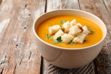 Tasty pumpkin cream soup with croutons and parsley in bowl on wooden table, closeup. Space for text