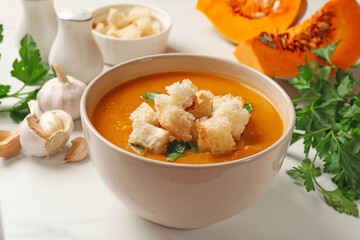 Tasty pumpkin cream soup with croutons and parsley in bowl on white table, closeup
