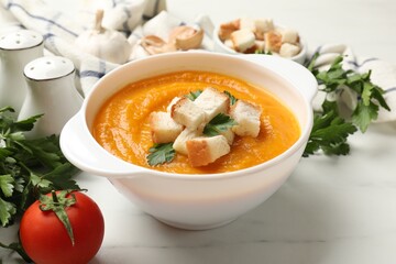Tasty pumpkin cream soup with croutons, parsley and tomato on white marble table, closeup
