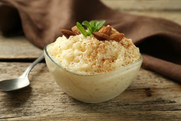 Delicious rice pudding with cinnamon, almonds and mint served on wooden table, closeup