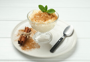 Delicious rice pudding with cinnamon, mint and spoon on white wooden table, closeup