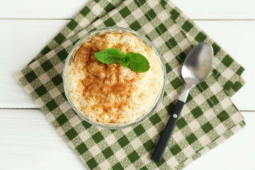 Delicious rice pudding with cinnamon, mint and spoon on white wooden table, flat lay