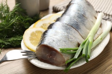 Pieces of delicious herring with lemon slices, green onions and dill on wooden table, closeup
