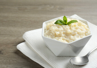 Delicious rice pudding in bowl, mint and spoon on wooden table, closeup. Space for text