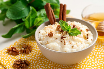 Delicious rice pudding with walnuts, cinnamon, mint and honey on table, closeup