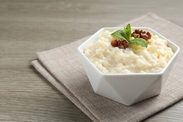 Delicious rice pudding with walnuts and mint in bowl on wooden table, closeup. Space for text