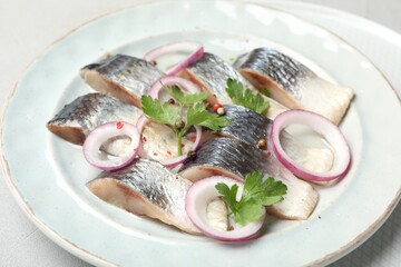 Pieces of delicious herring with spices and onions on white table, closeup