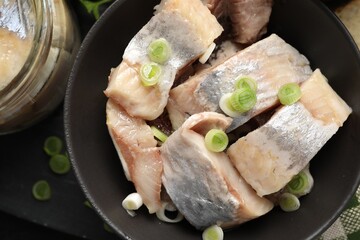 Pieces of delicious herring with green onions on black table, closeup