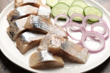 Pieces of delicious herring, onions and cucumber slices on table, closeup