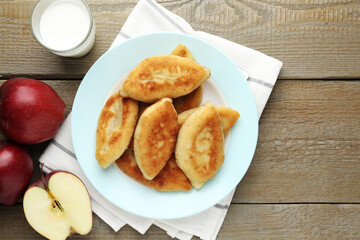 Delicious fried pyrizhky (stuffed pies) with apples and milk on wooden table, flat lay