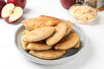 Delicious fried pyrizhky (stuffed pies) and apples on white wooden table, closeup