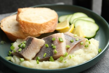 Pieces of delicious herring, mashed potato, cucumber slices and bread on black table, closeup