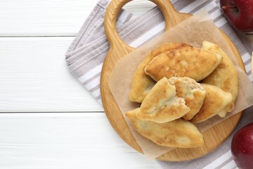 Delicious fried pyrizhky (stuffed pies) and apples on white wooden table, flat lay. Space for text