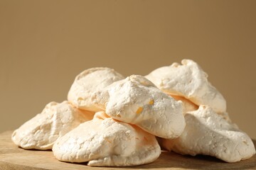 Delicious homemade meringue cookies on wooden table against beige background, closeup