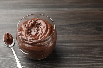 Delicious chocolate pudding in glass and spoon on wooden table, closeup. Space for text