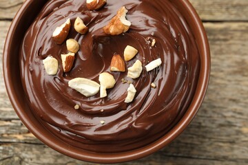 Delicious chocolate pudding with nuts in bowl on wooden table, top view