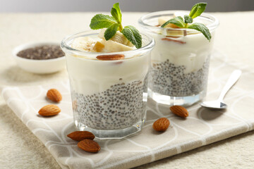 Delicious dessert with chia seeds, yogurt, banana, almond and mint in glasses on light textured table, closeup. Superfood