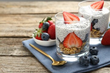 Delicious dessert with chia seeds, yogurt, granola, strawberries and blueberries on wooden table, closeup with space for text. Superfood