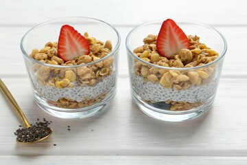 Delicious dessert with chia seeds, yogurt, granola and strawberries in glasses on white wooden table, closeup. Superfood