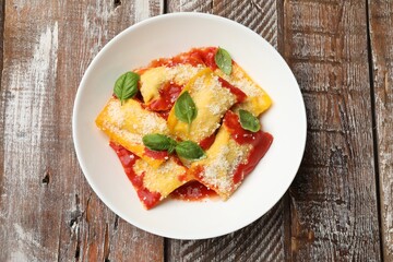 Delicious ravioli with tomato sauce, parmesan cheese and basil on wooden table, top view