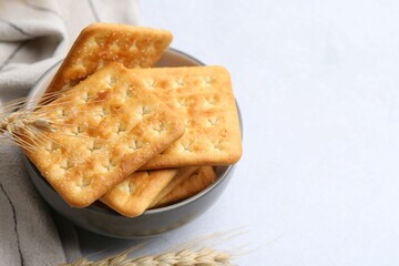 Tasty salty crackers with wheat spikes on white table, closeup. Space for text