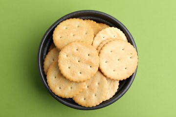 Tasty salty crackers on green background, top view
