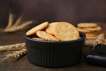 Tasty salty crackers and wheat spikes on wooden table, closeup