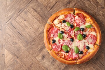 Tasty pizza with salami, cheese, basil and olives on wooden table, top view. Space for text