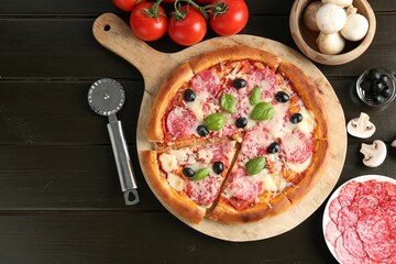 Tasty pizza, ingredients and cutter on black wooden table, flat lay. Space for text