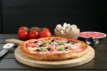 Tasty pizza, ingredients and cutter on black wooden table, closeup