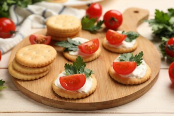Tasty crackers with cream cheese, tomatoes and parsley on white wooden table, closeup