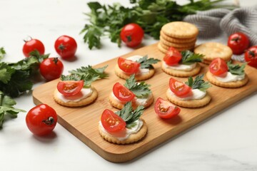 Tasty crackers with cream cheese, tomatoes and parsley on white table, closeup