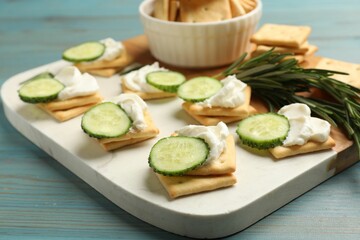 Tasty crackers with cream cheese, rosemary and cucumber on light blue wooden table, closeup