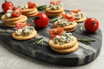 Tasty crackers with blue cheese, rosemary and tomatoes on grey textured table, closeup