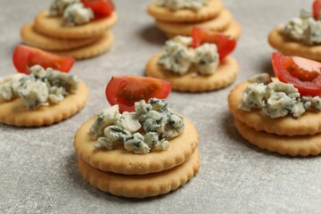 Tasty crackers with blue cheese and tomatoes on grey textured table, closeup